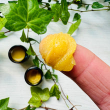 Balm of Gilead salve on a fingertip beside small tins of golden botanical balm.
