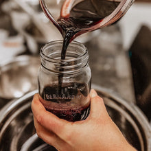 Hand-poured elderberry syrup being poured into a glass mason jar at The Green Goddess herbal workshop.