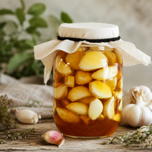 Jar of garlic cloves fermenting in raw honey with fresh garlic and herbs on a rustic wooden table